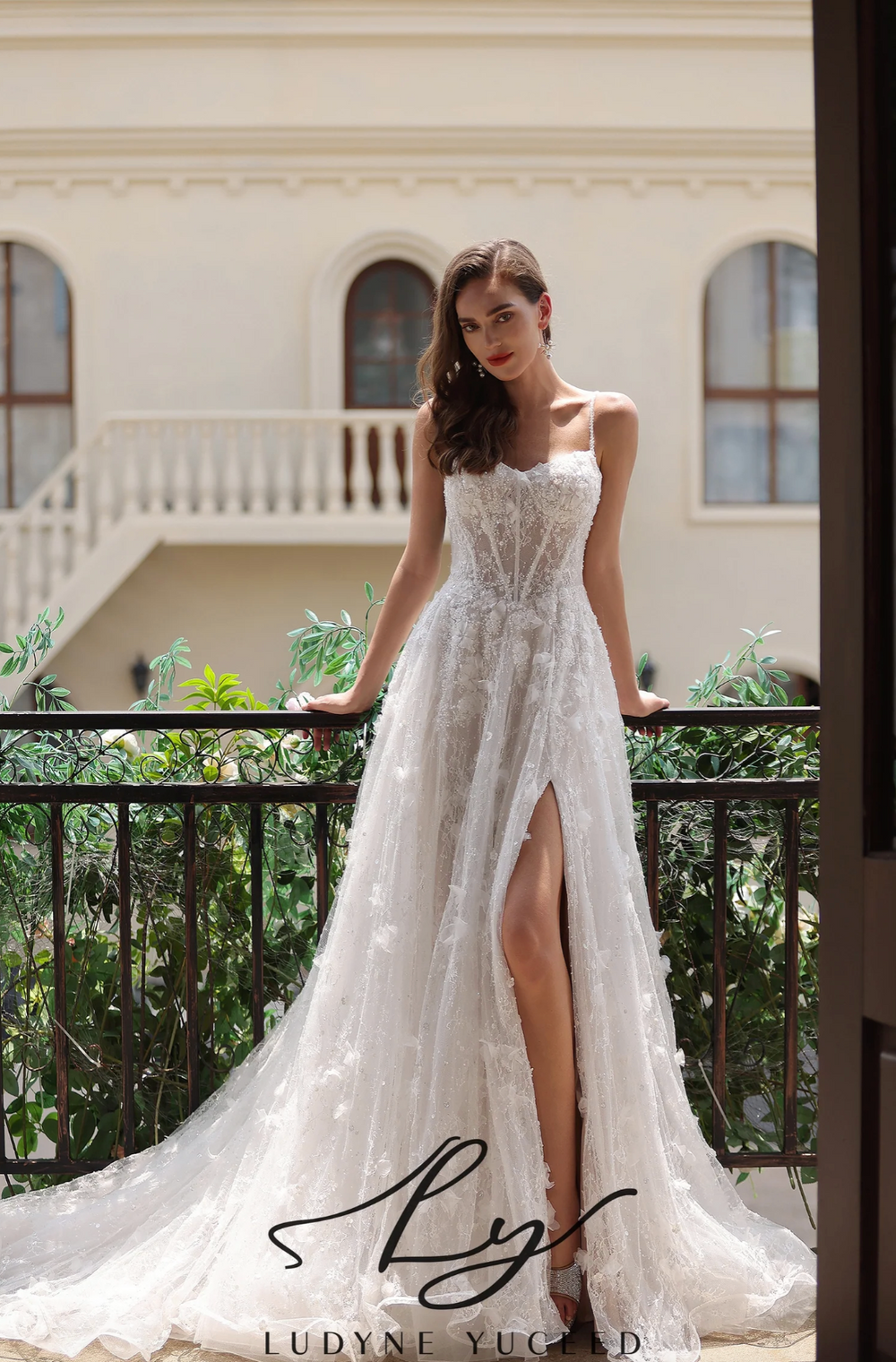 Romantic floral lace wedding gown with a high slit, spaghetti straps, and a flowing train, showcased outdoors.