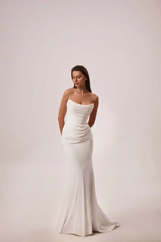 Woman wearing a strapless white wedding dress on a plain background