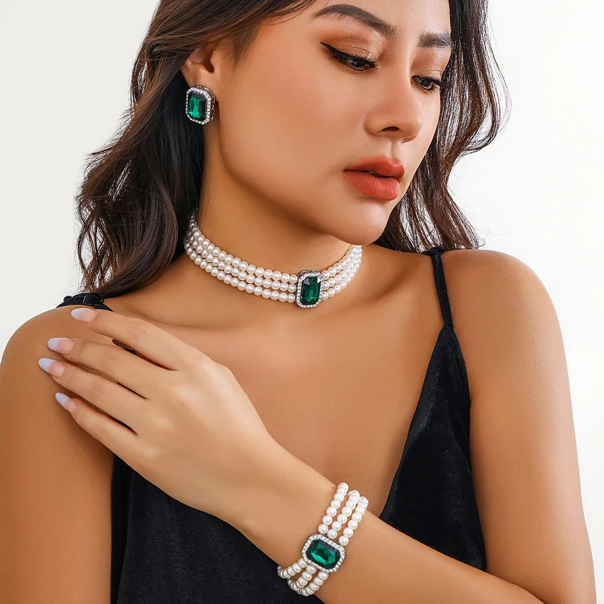 Woman wearing a pearl necklace, bracelet, and earrings with green gemstones on a white background