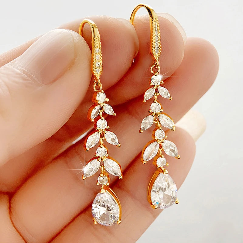 
                      
                        Gold earrings with clear gemstones held between fingers against a neutral background
                      
                    