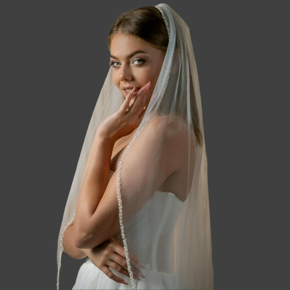 
                      
                        Woman wearing a white wedding dress with a veil against a neutral background
                      
                    