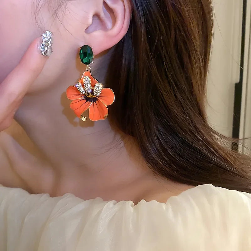 
                      
                        Close-up of a woman wearing an orange floral earring with a green gemstone.
                      
                    