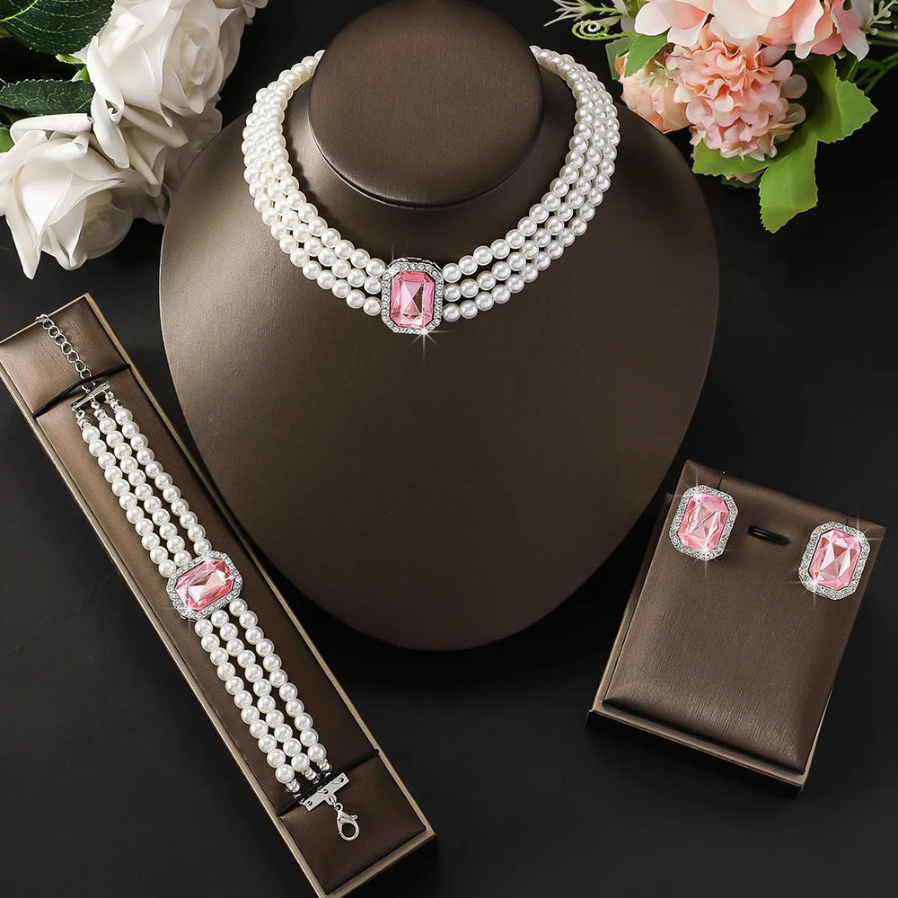 
                      
                        Pearl jewelry set with pink gemstones on a dark surface with flowers.
                      
                    