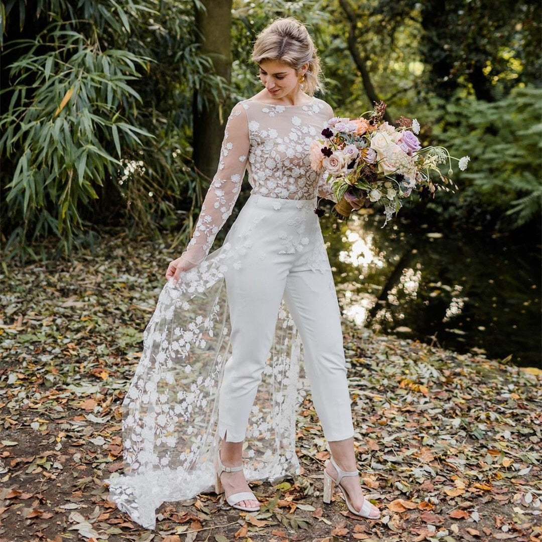 Girl Bride With Adorable Face In Beautiful Wedding Bridal White Dress And  Trousers High Heels Shoes Holding Full Skirt In Hands Posing On Background  Blooming Bush With Pink Flowers And Green Leaves